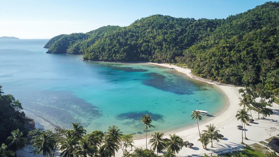 Luftaufnahme der Turtle Bay bei Tag mit weißem Strand, Riff und bewaldeten Hügeln