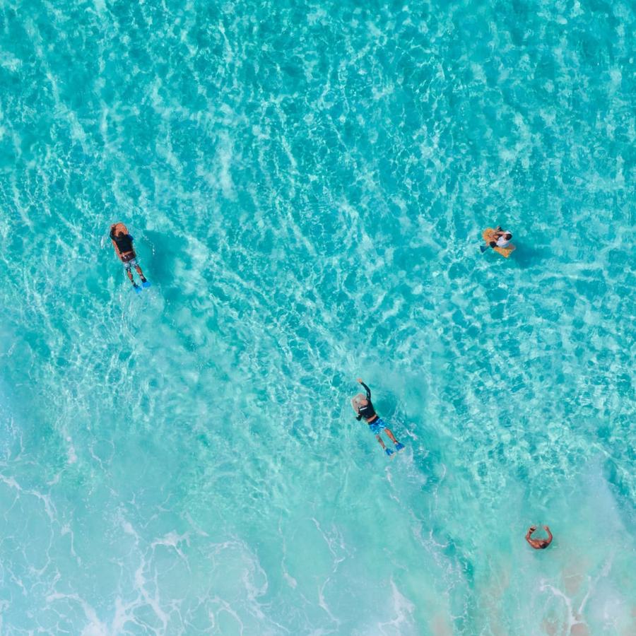 Luftaufnahme von Schwimmern im türkisen Wasser der Bucht