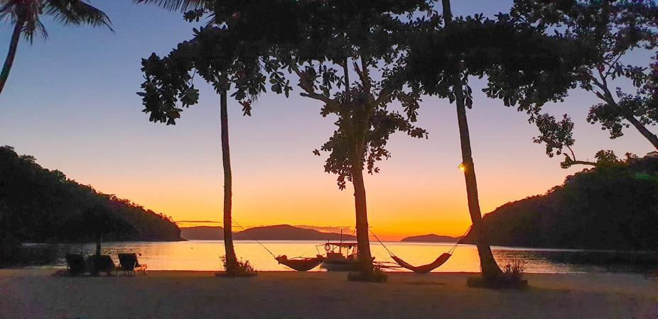 Sonnenuntergang über der Bucht mit Palmen im Gegenlicht