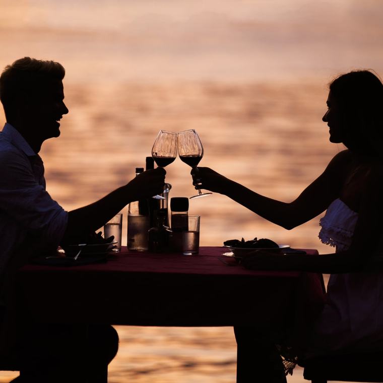 Zwei Gäste stoßen bei Sonnenuntergang am Strand mit Cocktails an
